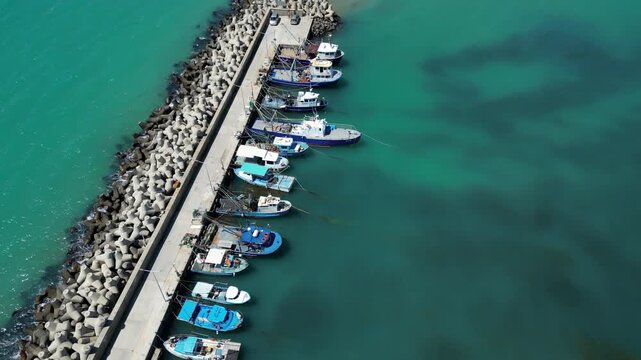 Aerial View of Fishing Boats Moored at Breakwater Pier in Blue Sea Water