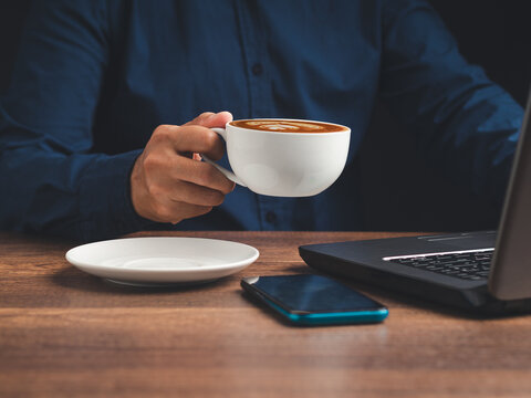Person holding coffee cup while working beside laptop 