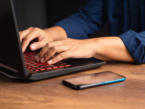 Person typing on laptop with smartphone on desk