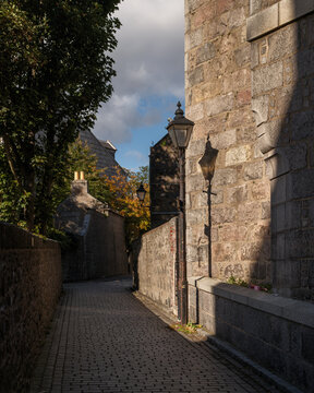 Cobbled lane lined with historic granite walls and vintage street lamps in Aberdeen City during a clear and sunny afternoon in Scotland