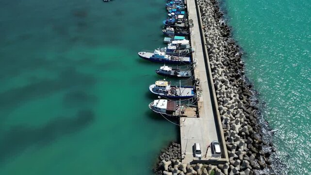 Aerial View of Fishing Boats Moored at Breakwater Pier in Blue Sea Water