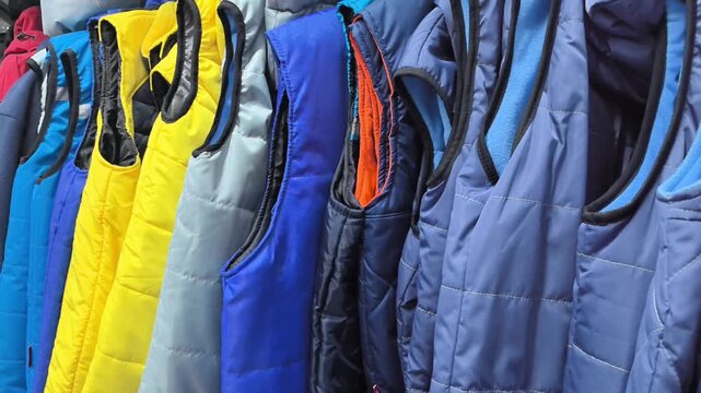 Numerous colorful vests are displayed in a clothing store, showcasing a variety of styles and fabrics. The vibrant colors and textures create a visually appealing arrangement.