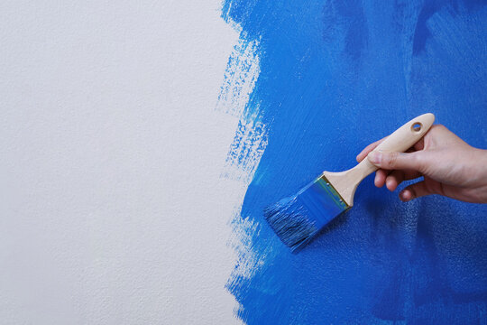 Paint brush, close up hand painter worker painting on surface wall Painting apartment, renovating with blue color paint. Leave empty copy space to write descriptive text beside.