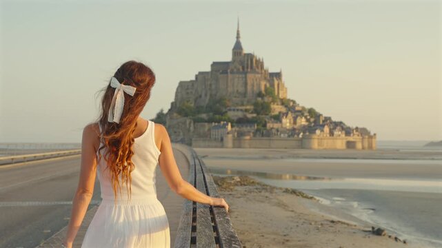 Woman in white dress walking toward Mont Saint Michel at low tide