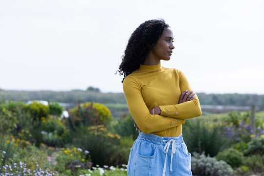 African American adult standing right in garden wearing mustard top and drawstring pants