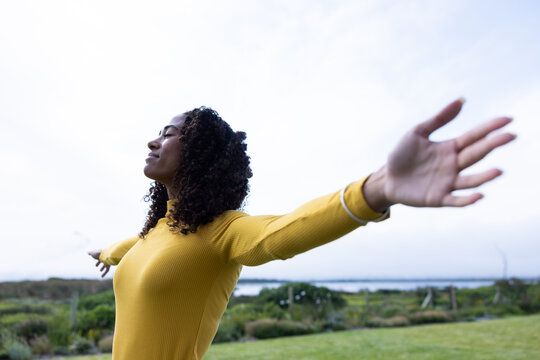 African American woman standing arms outstretched on coastal shore wearing yellow top, copy space