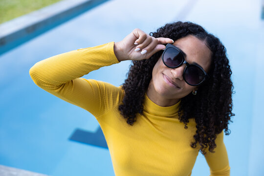 African American woman adjusting sunglasses standing at pool edge wearing yellow ribbed top