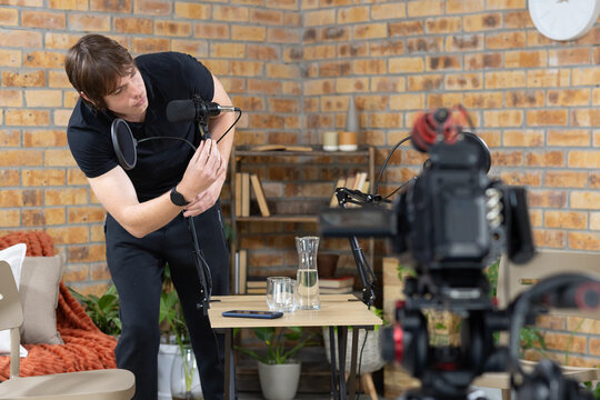 Man adjusting condenser microphone with pop filter on boom arm in cozy studio living room