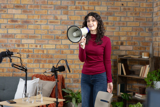 Woman standing holding megaphone, speaking into mic booms in studio, wearing burgundy sweater