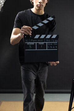 African American man in black tee holding slate, raising hinged top in dark studio with reflector
