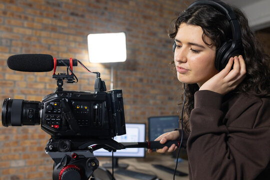 Adult female wearing headphones adjusting earcup while monitoring studio camcorder with shotgun mic
