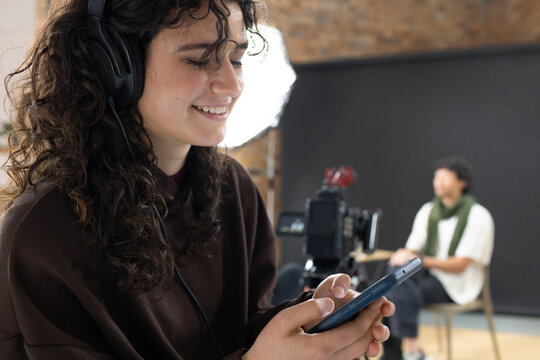 Crew recording in studio with woman wearing brown sweatshirt checking smartphone with headphones