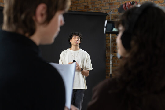 Indian actor in light tee and crew rehearsing in studio holding mic, script and phone rig
