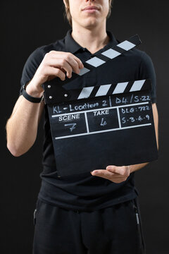 Male holding slate, lifting hinged top standing in studio wearing black polo, zip pockets