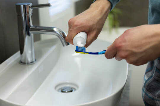 African American man squeezing toothpaste onto blue toothbrush at bathroom sink with chrome faucet