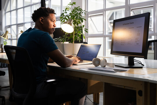 African American man working on laptop and external monitor at modern office desk with lamp