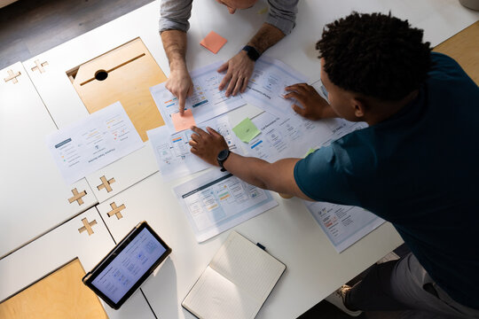 Diverse male coworkers leaning over modular table moving UX wireframes and sticky notes