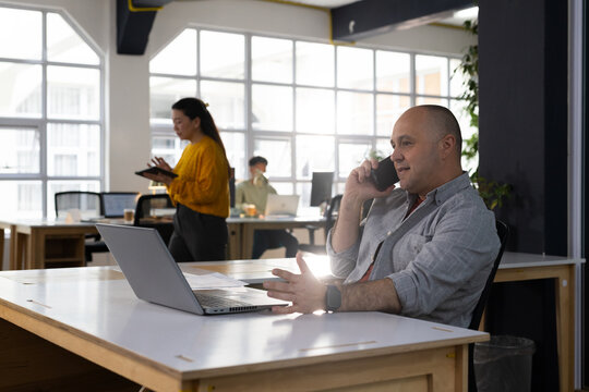 Diverse coworkers talking and working in open office, using laptop, smartphone, tablet, copy space