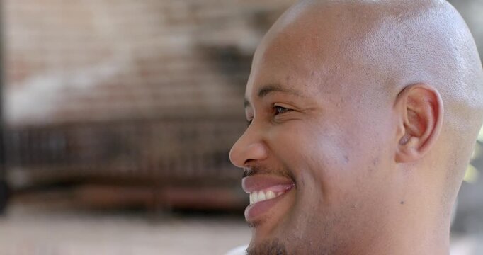 Adult African American man smiling, turning to camera following cue on porch with brick wall bench