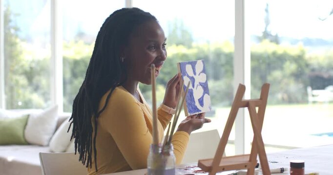African American woman presenting canvas after painting, high-fiving and placing on easel by window