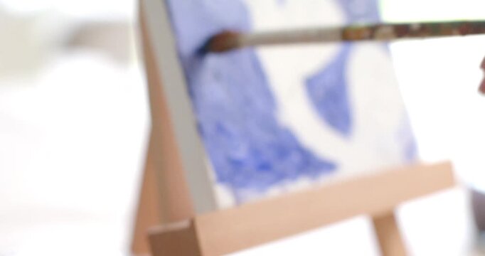 Brush is pressing into blue paint, mixing and applying strokes on tabletop easel to fill background