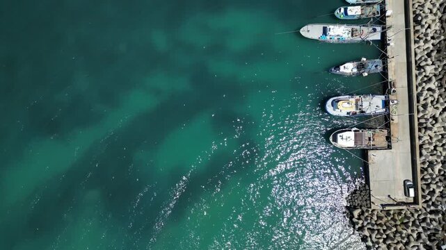Aerial View of Fishing Boats Moored at Breakwater Pier in Blue Sea Water
