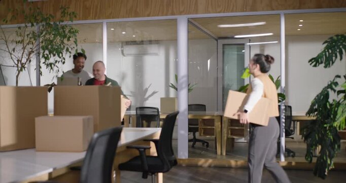 Diverse coworkers spotting cardboard boxes, unpacking, placing plant, lamp, screen