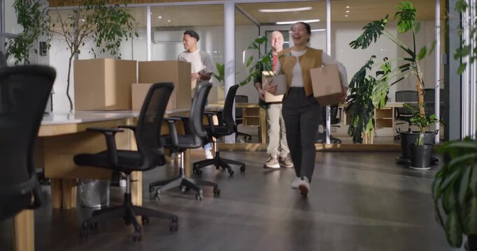 Diverse coworkers moving in, carrying boxes into modern office, placing boxes and arranging plants
