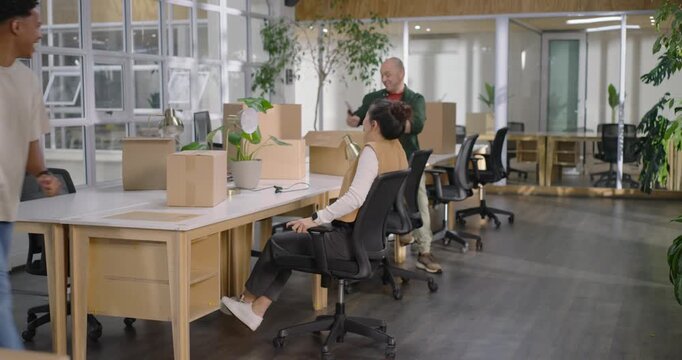 African American man pushing Asian woman in rolling chair while colleague recording in office setup