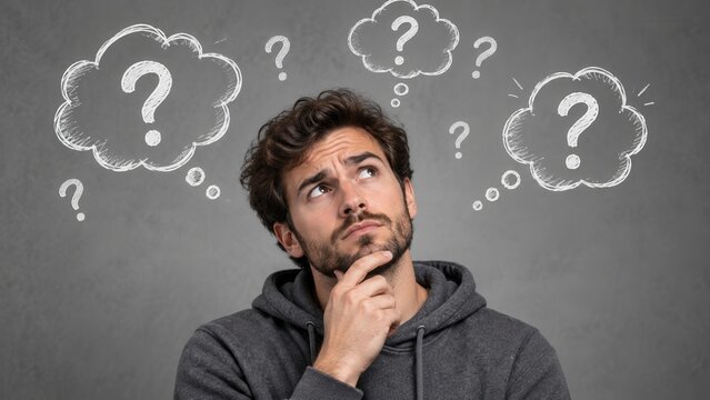 Confused young man thinking with question marks and thought bubbles on gray background