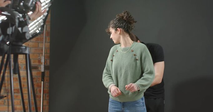 African American woman in green top receiving windscreen while crew adjusting mic pack in studio