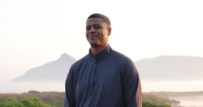 Adult man facing camera on bluff by mountain peak smiling, grinning, glancing down, returning gaze