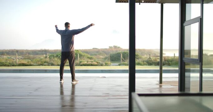 Man in grey top stretching on poolside deck morning sun, raising palms overhead, lowering to chest