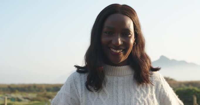 Mid-adult woman posing as camera widens, tucking hair, crossing arms in white knit sweater on coast