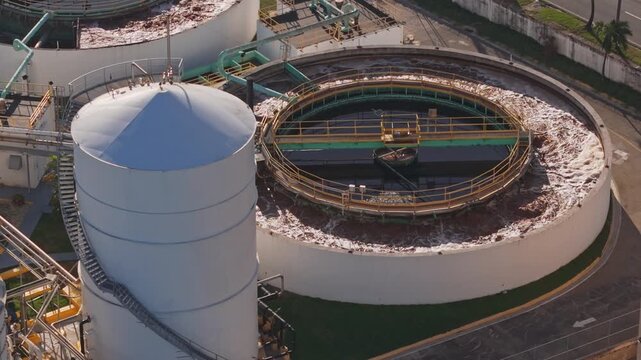 High-angle aerial drone view of industrial water treatment plant clarifier tanks and storage silos