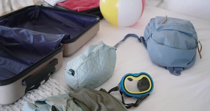 Camera is panning left, showing open hardshell suitcase on bed with travel gear for packing