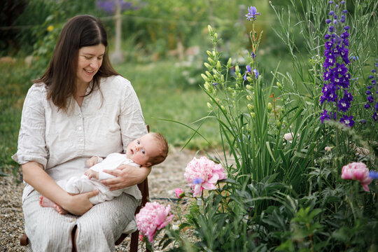 Mother hugging cute newborn baby among flowers in the garden. Love, care and family in countryside concept. Happy Mothers day! Adoption and maternity