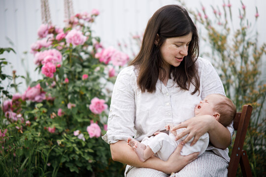 Mother hugging cute newborn baby among flowers in the garden. Love, care and family in countryside concept. Happy Mothers day! Adoption and maternity