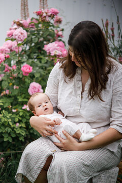 Mother hugging cute newborn baby among flowers in the garden. Love, care and family in countryside concept. Happy Mothers day! Adoption and maternity