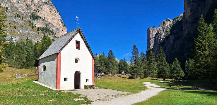 The winding Vallunga hiking trail among the rocks with a church in the Puez Geisler nature park in Selva. Panorama.