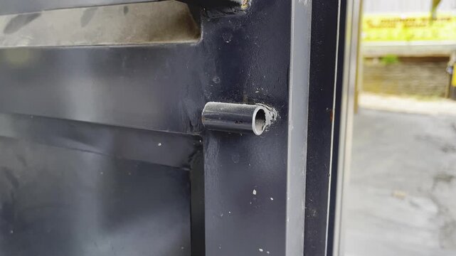 Close up view of a metal cylinder hinge welded on a black gate