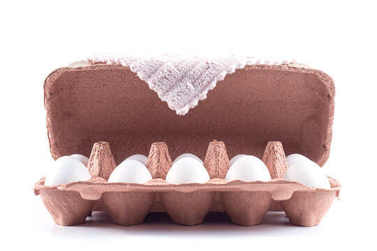 White eggs in an open brown carton with a fabric towel against a white background. Food ingredient and grocery packaging for poultry product advertising, recipe content and supermarket promotions.