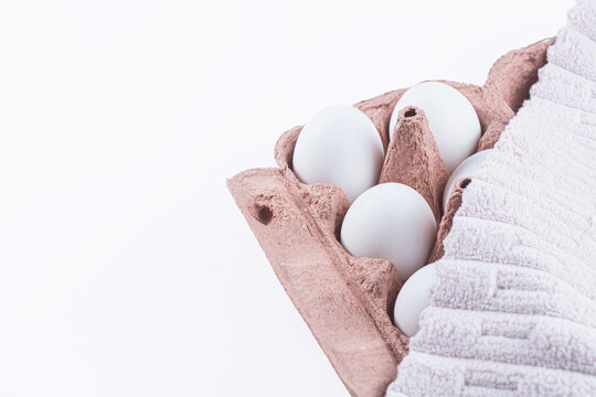 Fresh white chicken eggs in cardboard tray covered with kitchen towel isolated on white background. Organic farm eggs, grocery staple, kitchen storage, baking preparation and food staging concept.