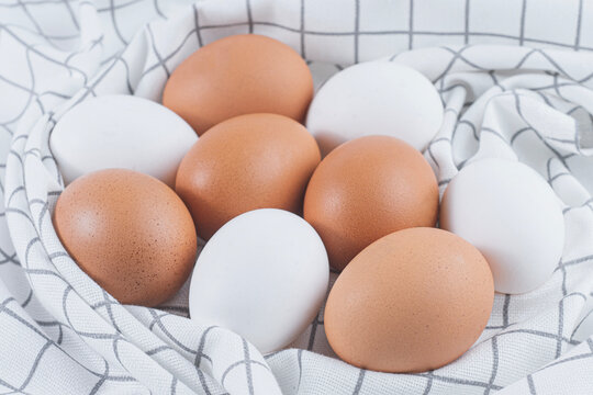 Fresh white and brown chicken eggs on plaid kitchen towel cloth. Organic farm eggs, protein food, baking ingredients, domestic kitchen setup and food staging concept.