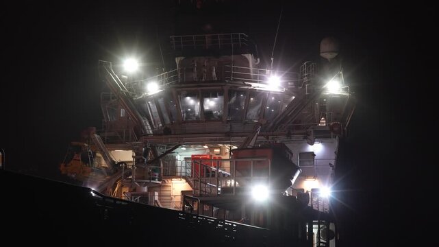 Bright work lights illuminate the bridge and upper decks of a large industrial vessel at night, oil tanker or professional commercial boat