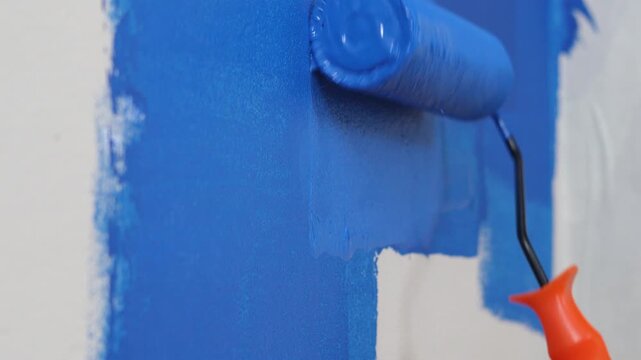 Roller Brush Painting, Worker painting on surface wall Painting apartment, renovating with blue color paint. Leave empty copy space white to write descriptive text beside.