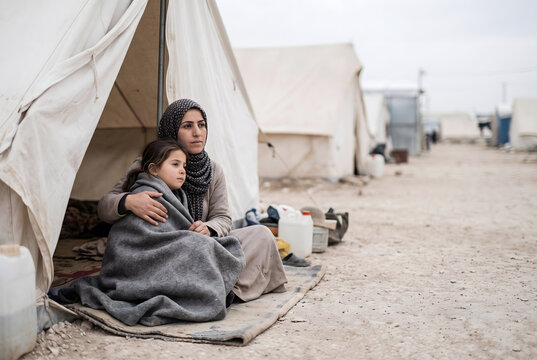 Displaced mother and daughter sitting outside a refugee camp tent