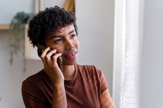 African American woman talking on phone indoors near window and plant
