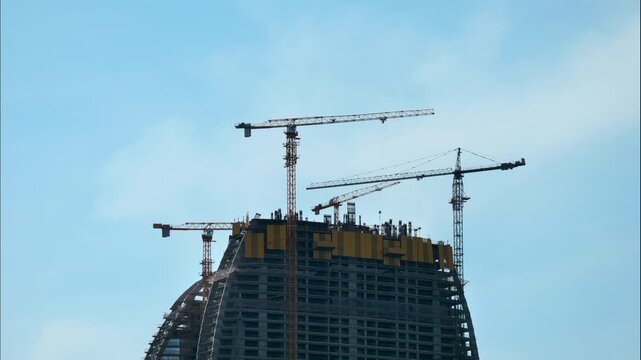 Skyscraper construction timelapse with tower cranes rotating and lifting materials above unfinished high-rise building with concrete floors and steel reinforcement during urban real estate development