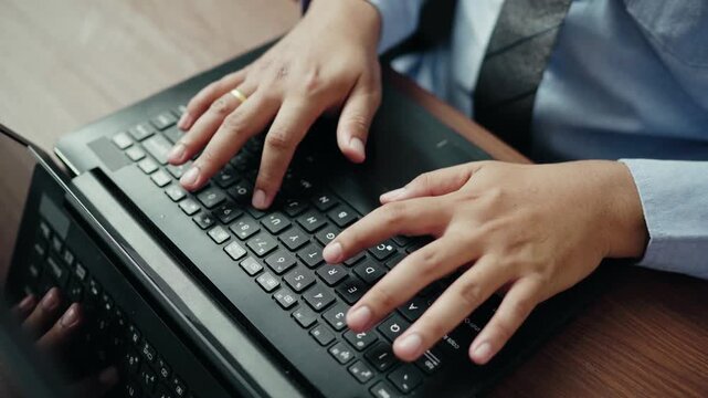 Businessman typing on black laptop keyboard at office, professional workflow, data entry, work efficiency
